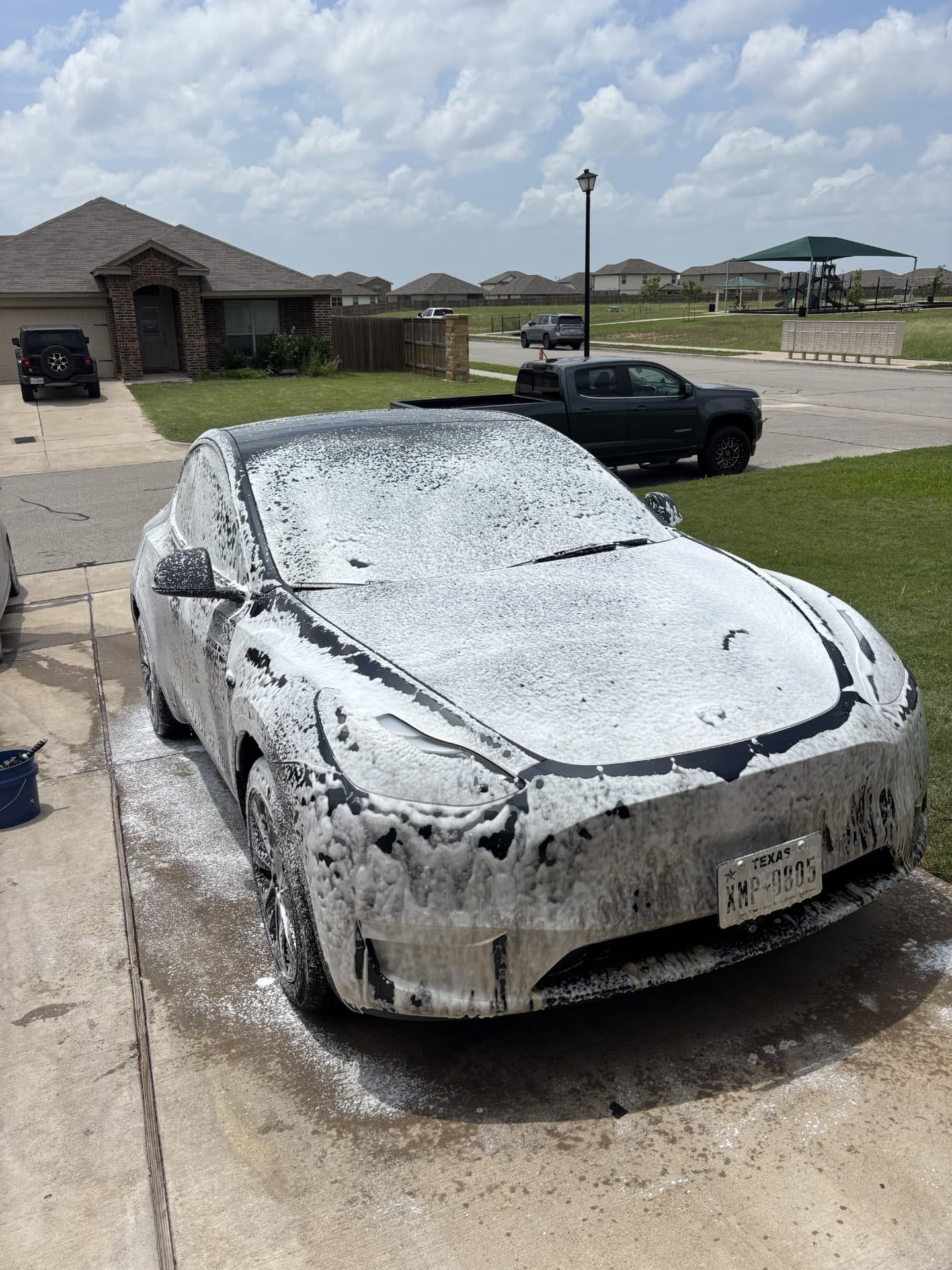 Black Tesla Model Y covered in thick foam soap during a hand wash